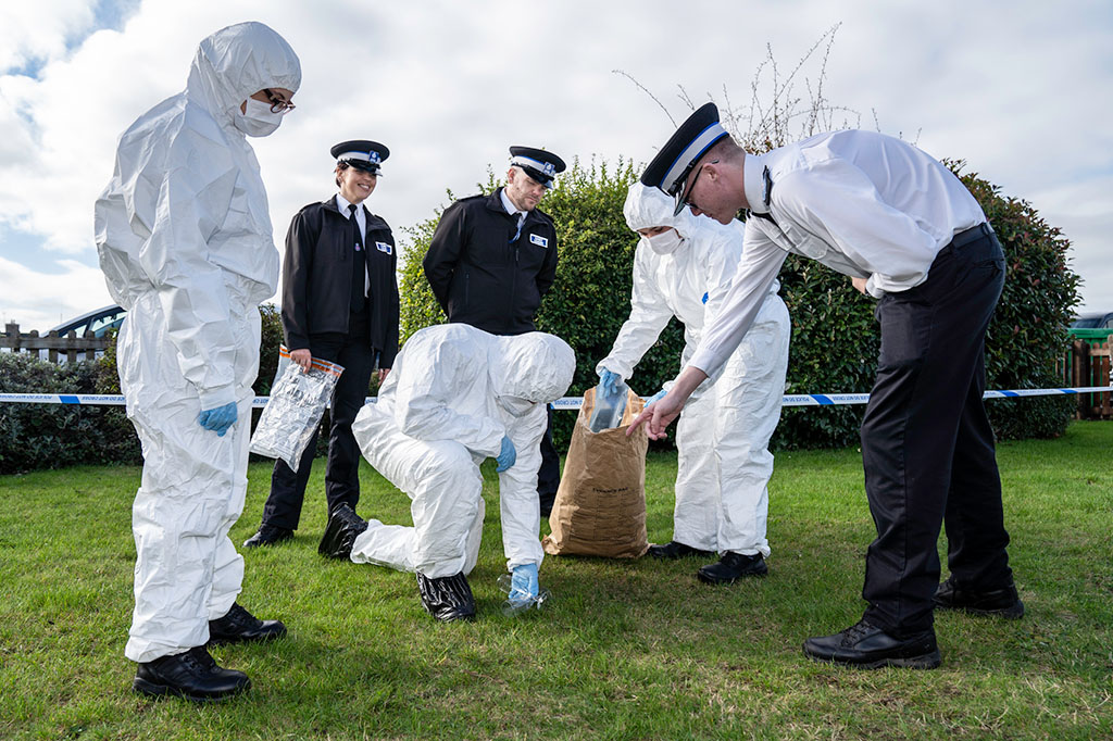 police cadets dressed in forensic suits as part of pretend crime scene and cadet leaders talking them through what they need to do