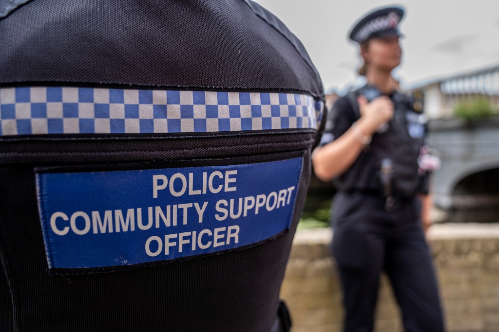 Back of PCSO jacket with police officer in uniform in the background