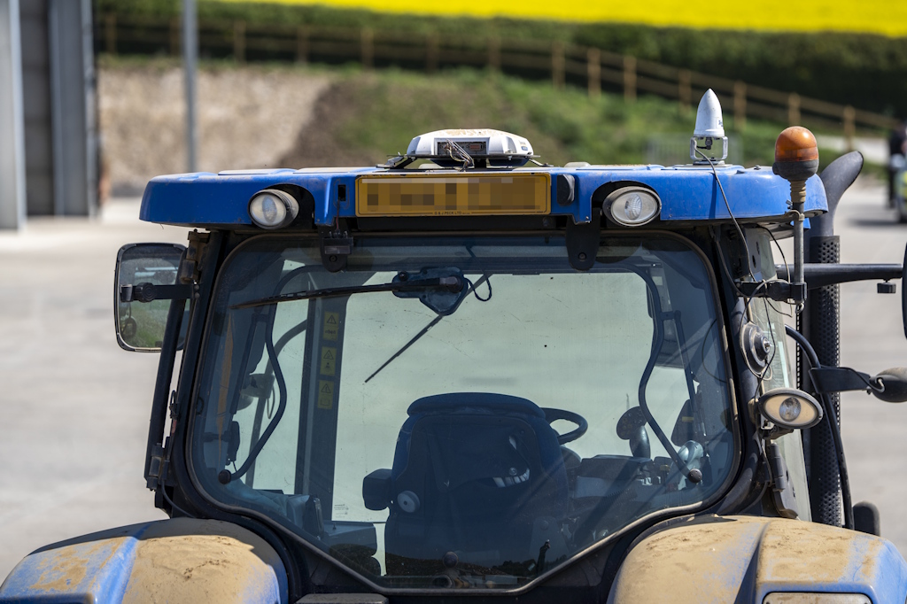 A blue tractor cab with GPS equipment fitted. There is a field of mustard in the distance