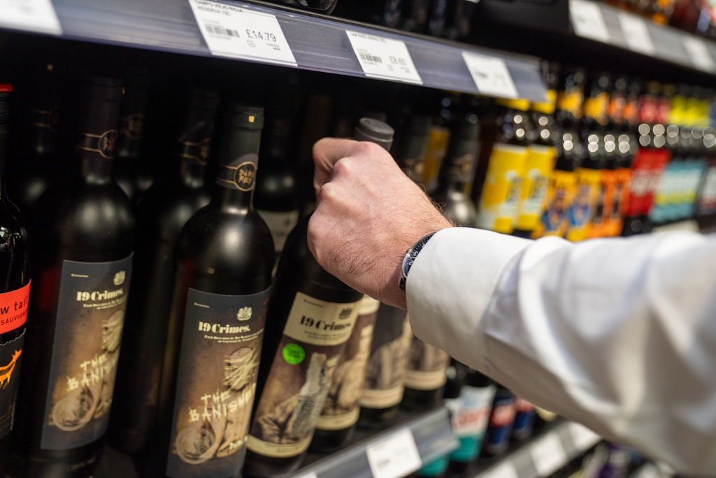 A hand picking up a wine bottle from a chiller cabinet