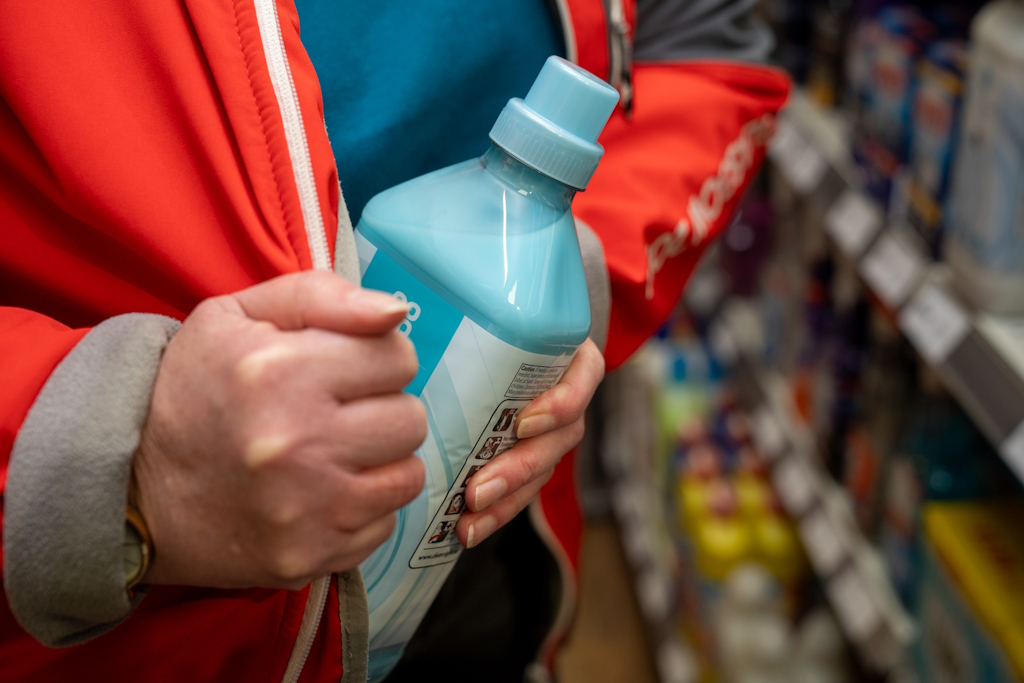 A hand places a bottle of washing liquid inside a red coat