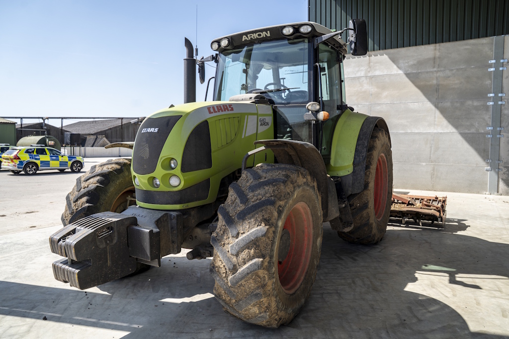 A lime green tractor parked in a farm yard with an Essex Police liveried vehicle in the background