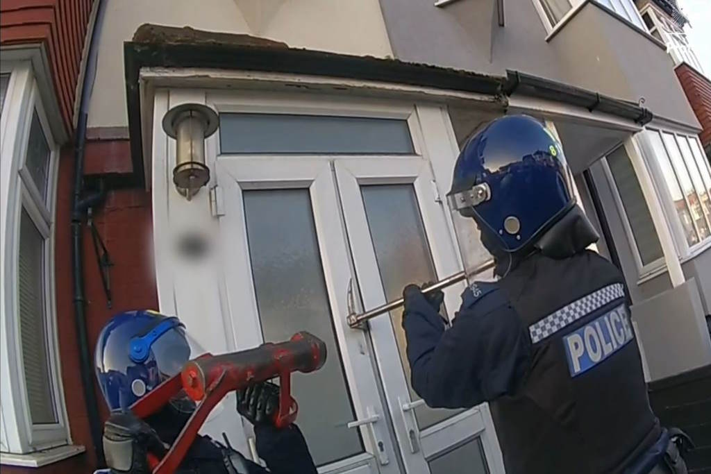 Two uniformed police officers force entry to front door