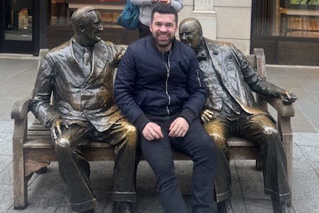 Arlind Xhokola wearing dark clothing sits on a bench between two statues