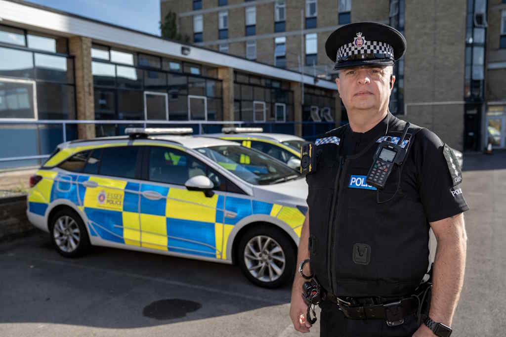 A police officer in police uniform standing in front of a marked police car