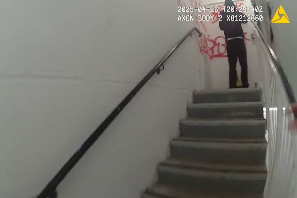 Flight of stairs with hooded figure at the top, graffiti on wall in background
