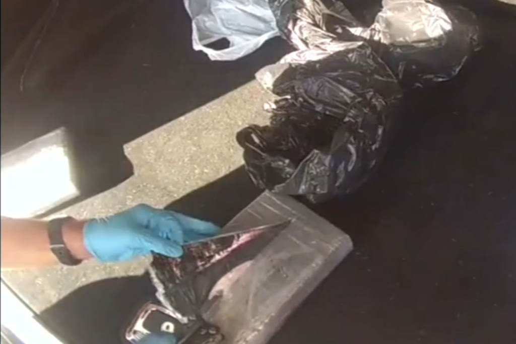 A gloved hand opens a brick package of cocaine