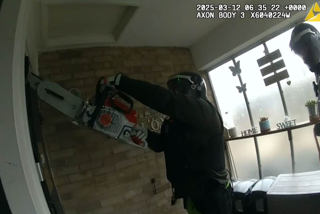 Officer chainsaws through a door
