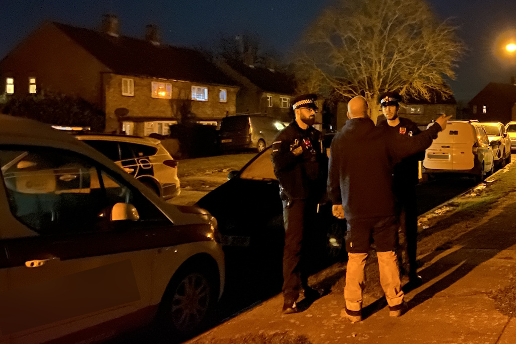 Two uniformed Essex Police local policing officers talk to a man in a residential street at night