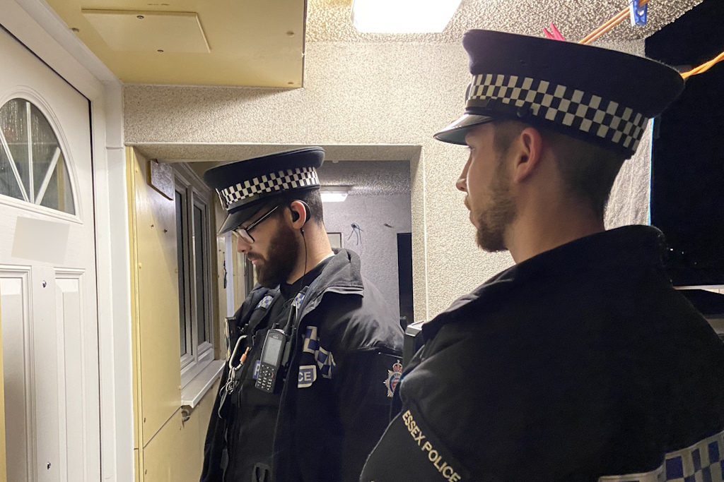 Two uniformed Essex Police local policing officers knock on the front door of a flat