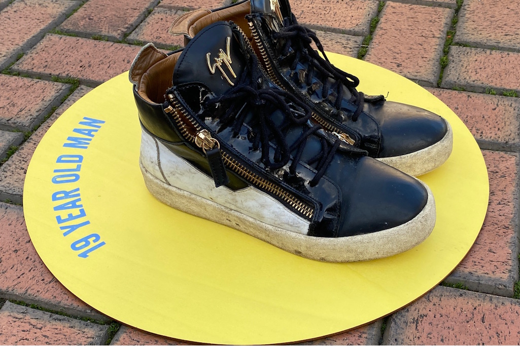 Black and white shoes belonging to 19 year old man sitting on yellow circle with writing on left side