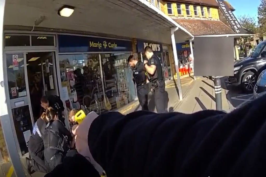 Officers restrain a man outside a row of shops