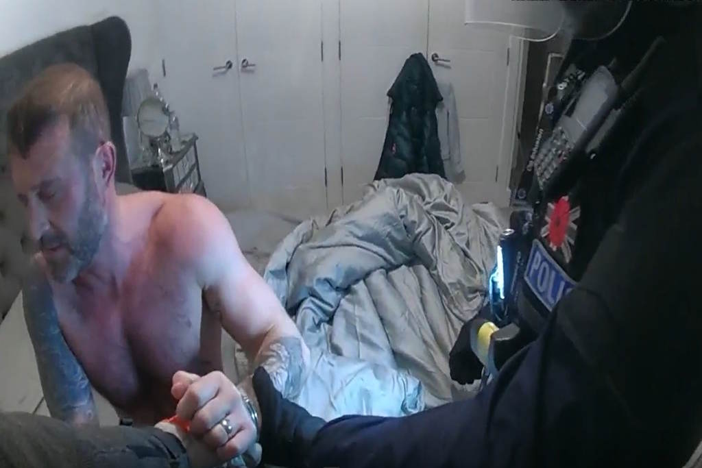 A topless man is placed in cuffs as he sits on a bed