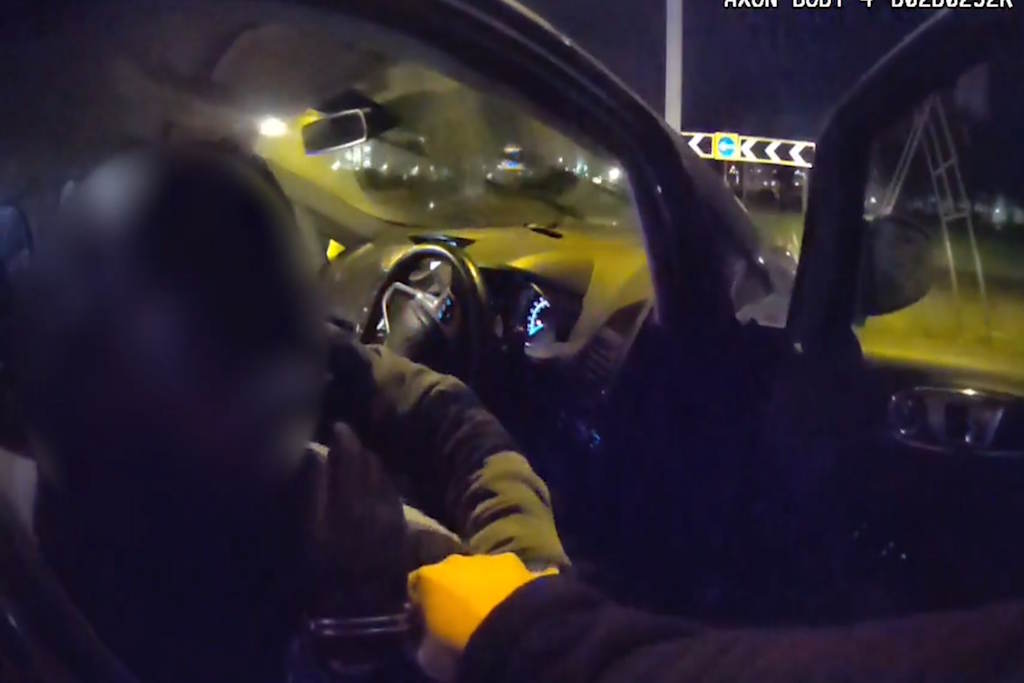 A gloved man in handcuffs at the wheel of the vehicle, captured on officer's Body Worn Video
