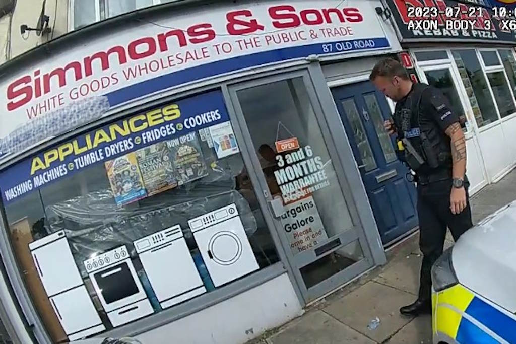 A uniformed officer walks outside a shop bearing the sign Simmons and Sons