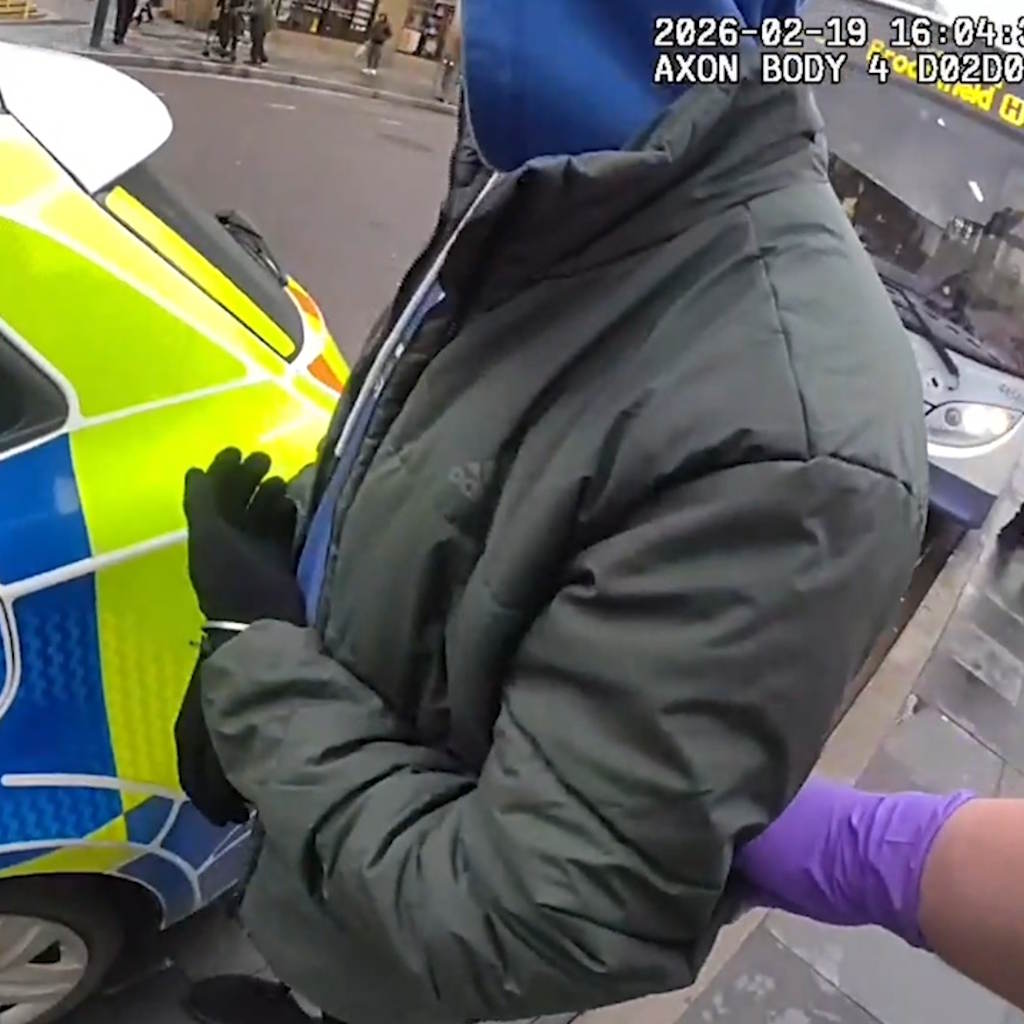 A man in a green jacket, wearing black gloves, in handcuffs