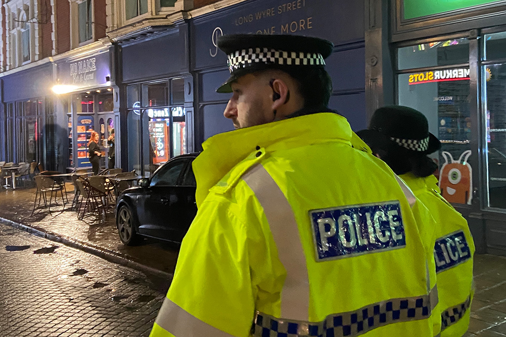 Essex Police officers on foot patrol along a busy night-time street in Colchester.