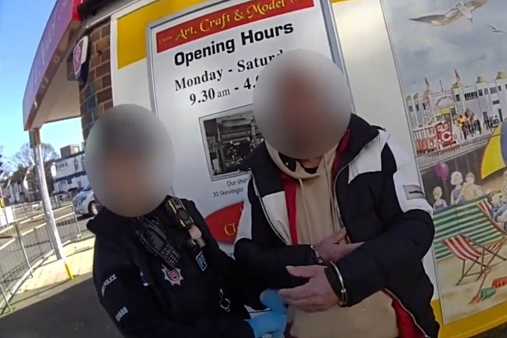 An officer stands next to a man wearing handcuffs
