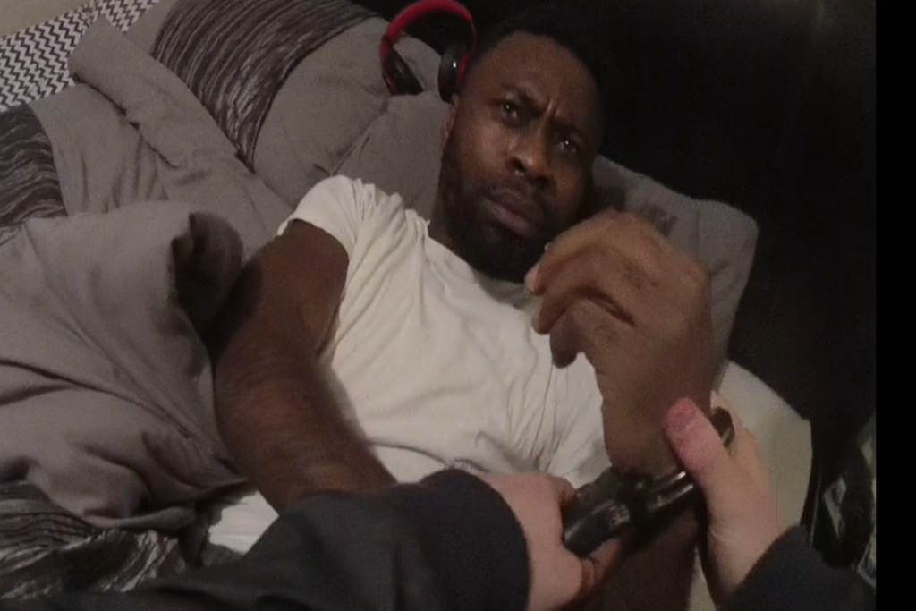 A man wearing a white T-shirt in handcuffs