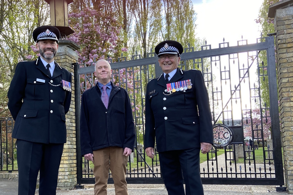 Three men, two in Essex Police ceremonial uniform, stand in front a pair of decorative, wrought iron gates leading to a memorial garden