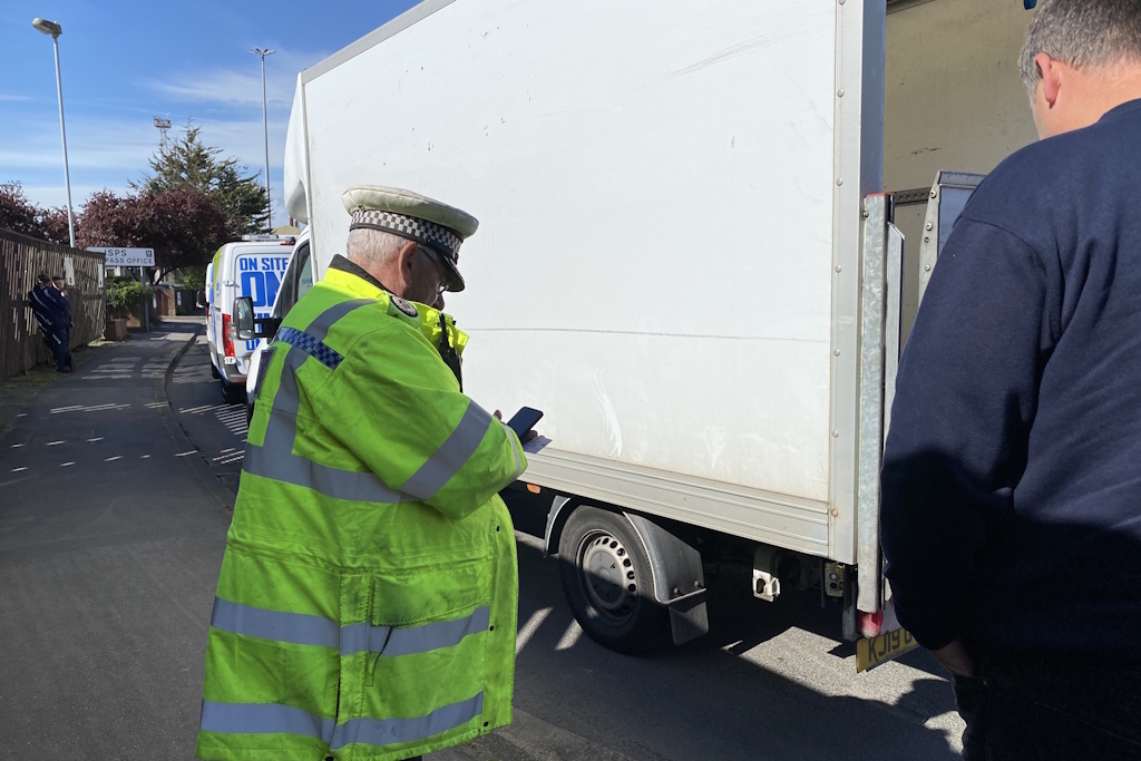 A volunteer Essex Police special constable in a yellow fluorescent jacket speaks with a lorry driver by the side of a road