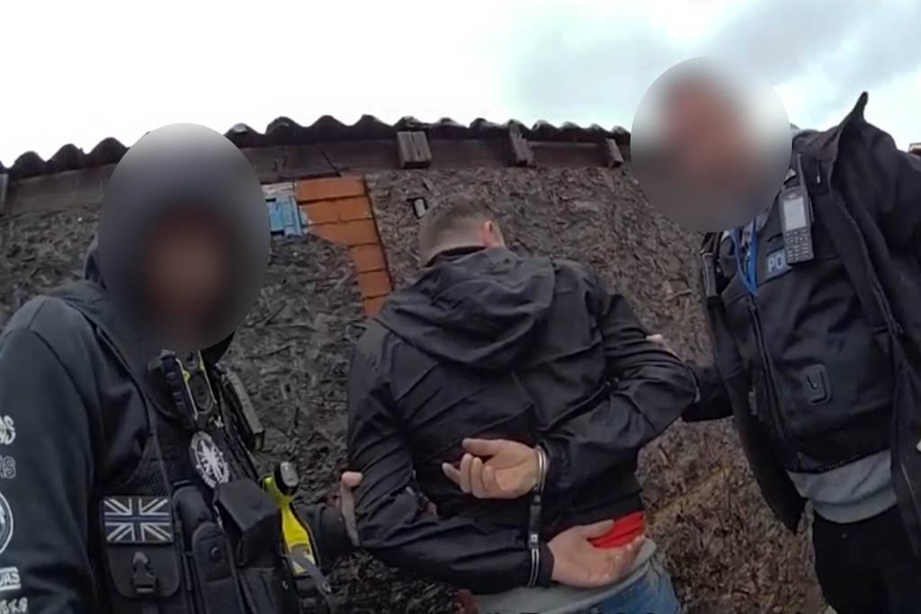 A man in dark clothing is held in handcuffs by two police officers
