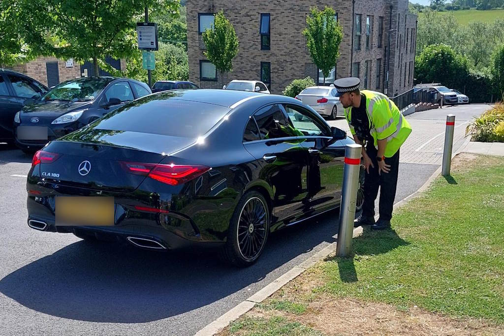 An officer leans in to speak through the open window of a black car