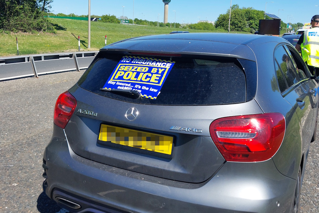 A vehicle seized by police with a sticker in its back window, which states: No Insurance. Seized by police. Stay insured. It's the law. askMID.com  