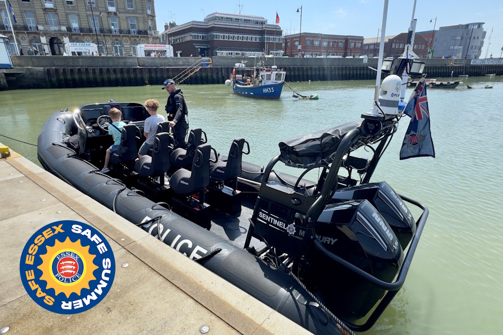 An Essex Police rigid-hulled inflatable boat, or rib, moored alongside a pier. Two children are on the rib, speaking with a uniformed Essex Police marine officer. The image includes an Essex Police logo, stating Safe Essex, Safe Summer