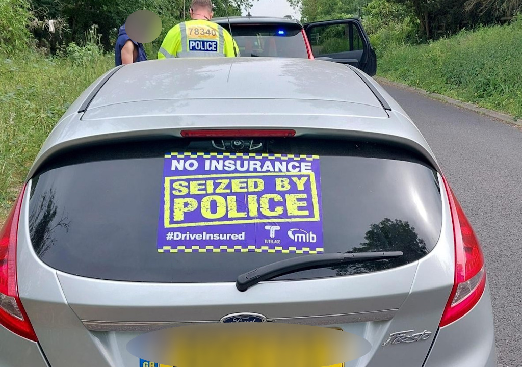 A seized car with an officer talking to a man in the background.