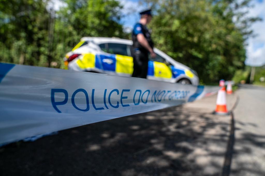 Police tape in foreground with officer and car blurred behind