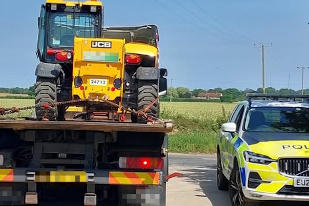A yellow telehandler on a pick-up truck parked next to a liveried Essex Police vehicle