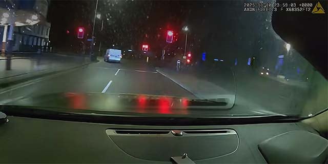 View from police car in pursuit of white van going through red traffic lights