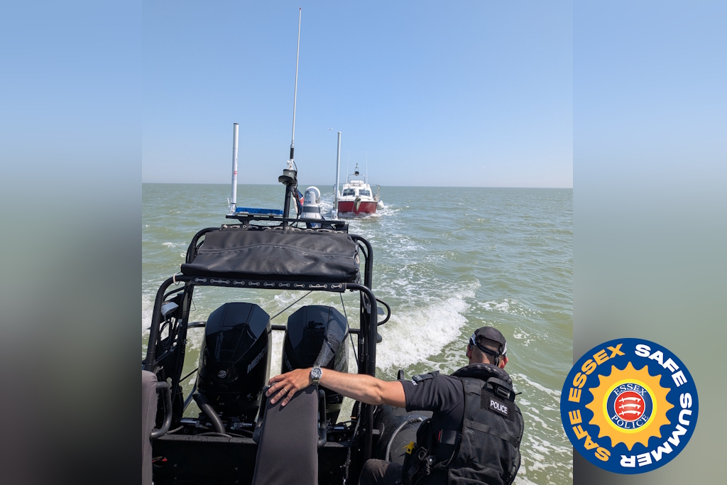 A police officer on a rigid-hulled inflatable boat, or rib, towing a small red and white motorboat at sea on a sunny day, with an Essex Safe Summer campaign logo in the corner of the picture