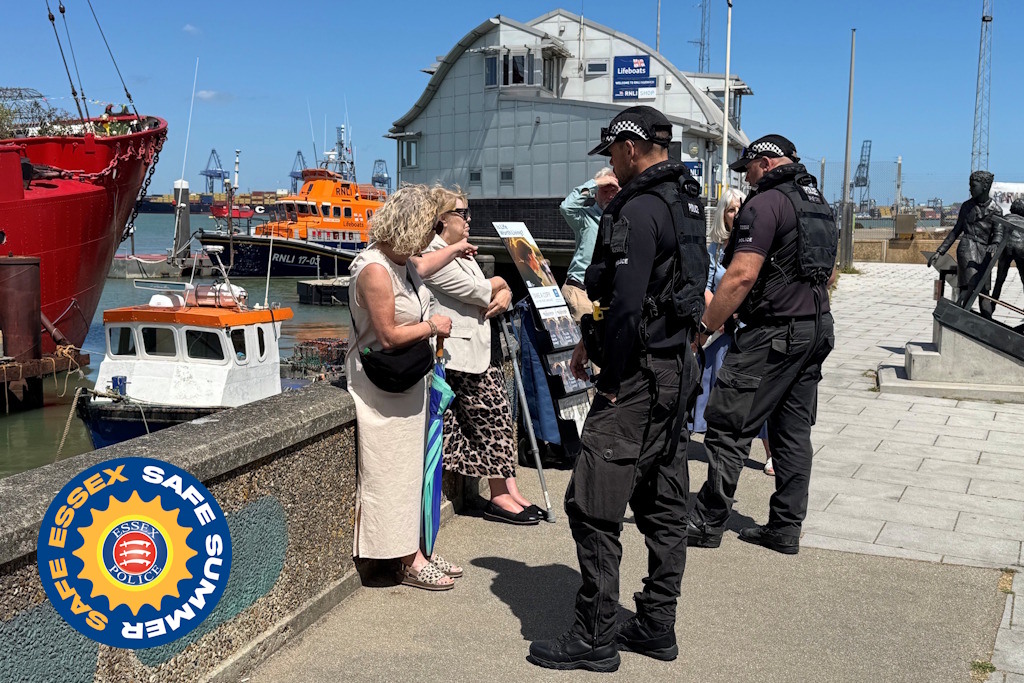A uniformed Essex Police Marine Unit officer speaking with two women on a sunny quayside near a lifeboat station
