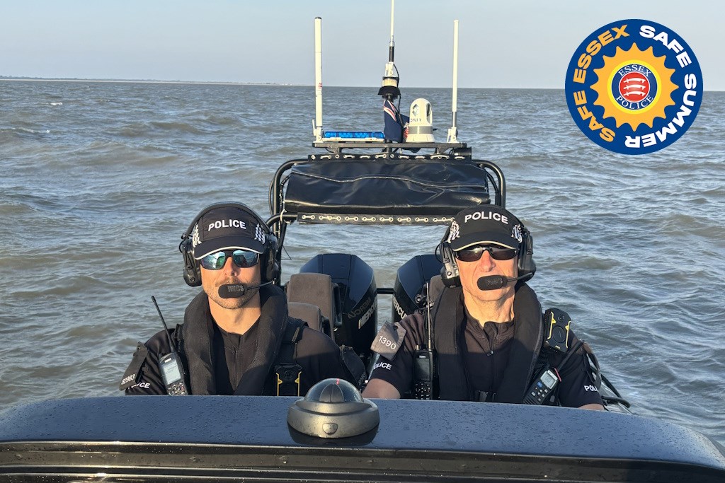 Two Essex Police marine officers in uniform and life jackets on a rigid-hulled inflatable boat at sea, with an Essex Safe Summer campaign logo in the corner of the picture