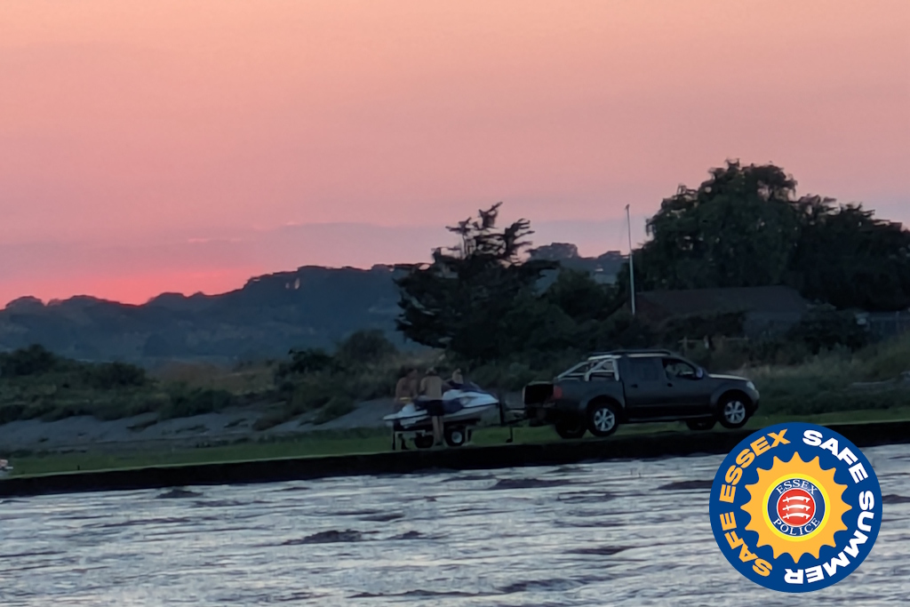 A pick-up truck towing a personal watercraft on a slipway at sunset - which is a beautiful pink - with an Essex Police Safe Summer logo in the corner of the image