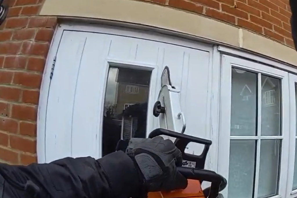 An officer uses a chainsaw on a white door
