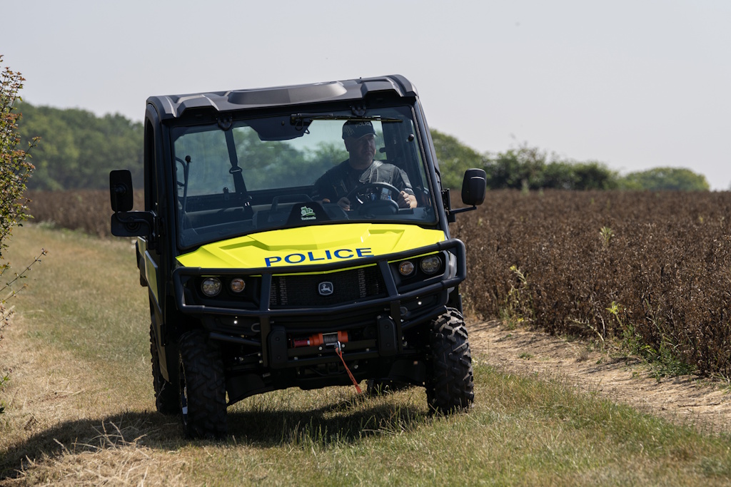 A uniformed Essex Police rural engagement officer driving an Essex Police liveried John Deere Gator utility vehicle along a rural track towards the camera