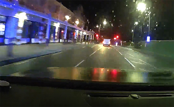 Dashcam footage showing a car ahead on a town-centre road at night.