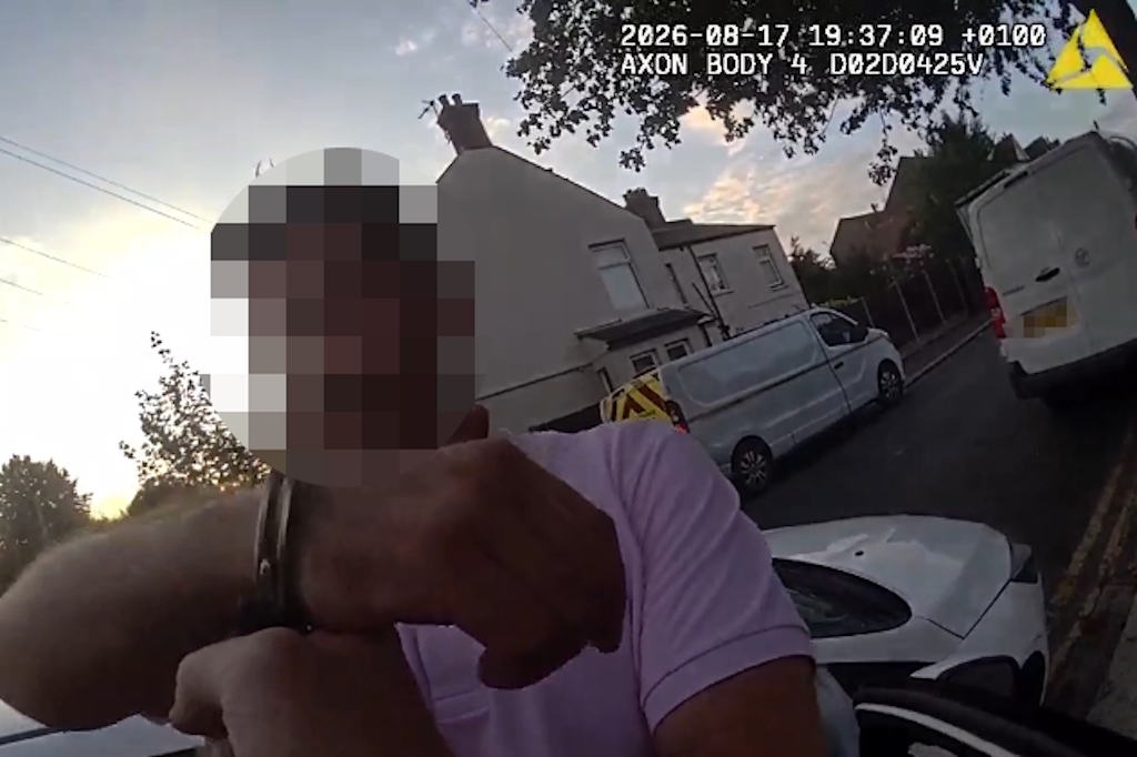 Essex Police body-worn video still of a man in handcuffs beside a car, with a liveried Essex Police vehicle in the background