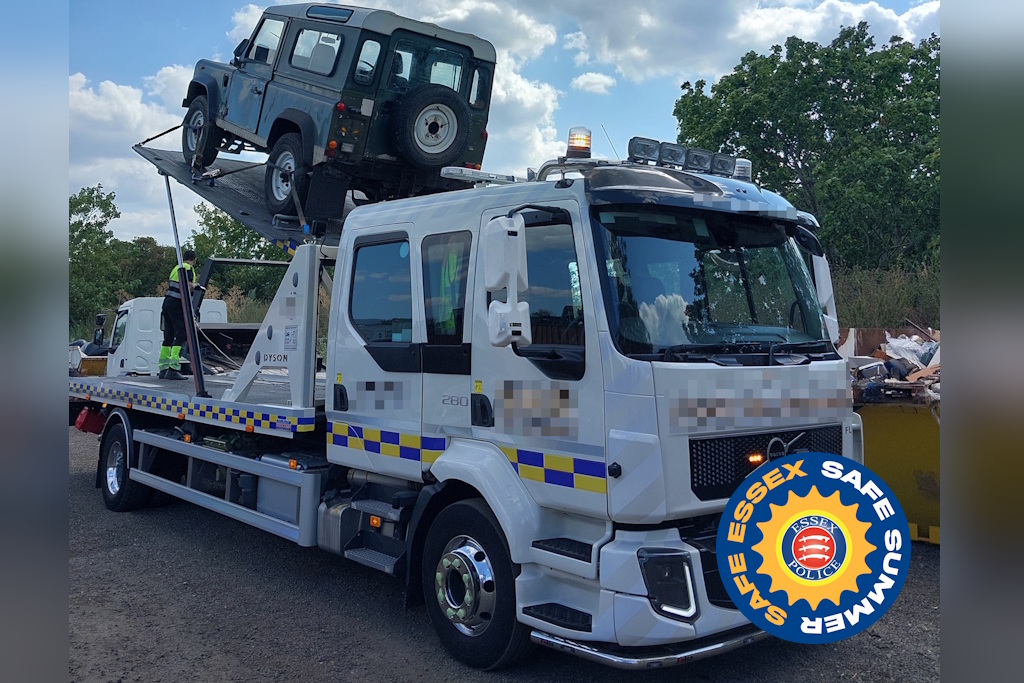 A white recovery truck carrying a green Land Rover Defender, with a person in high-visibility gear on the flatbed