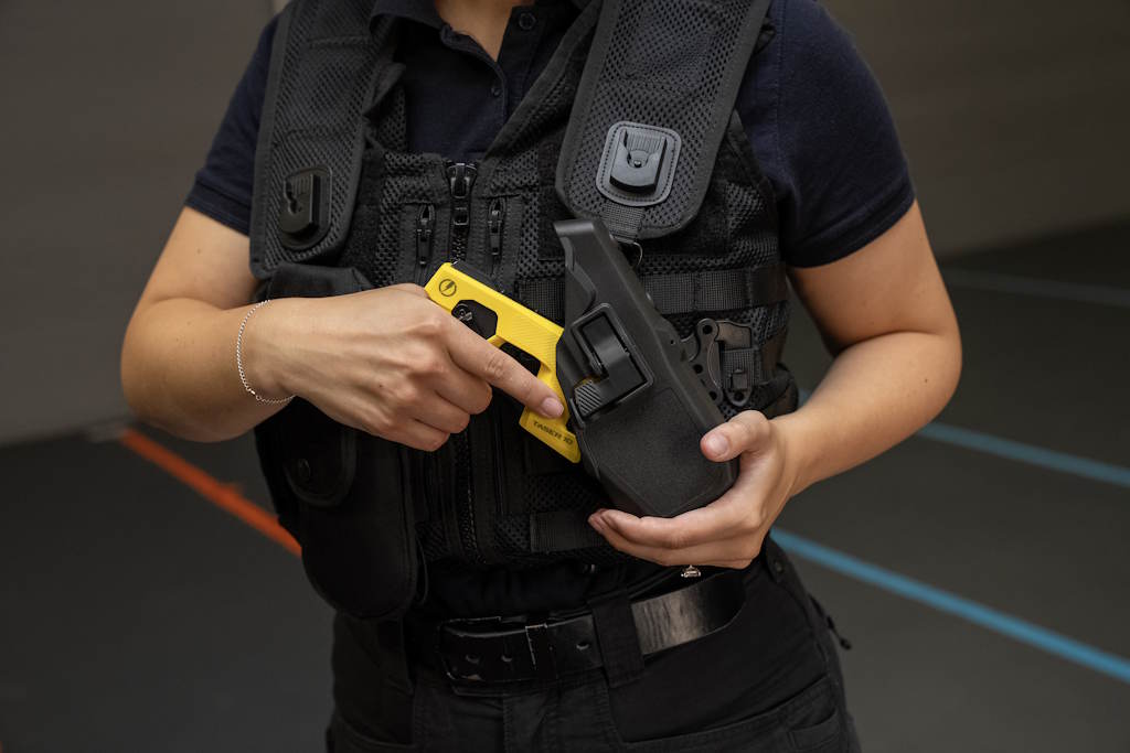 A uniformed police officer draws a yellow Taser device from a holster