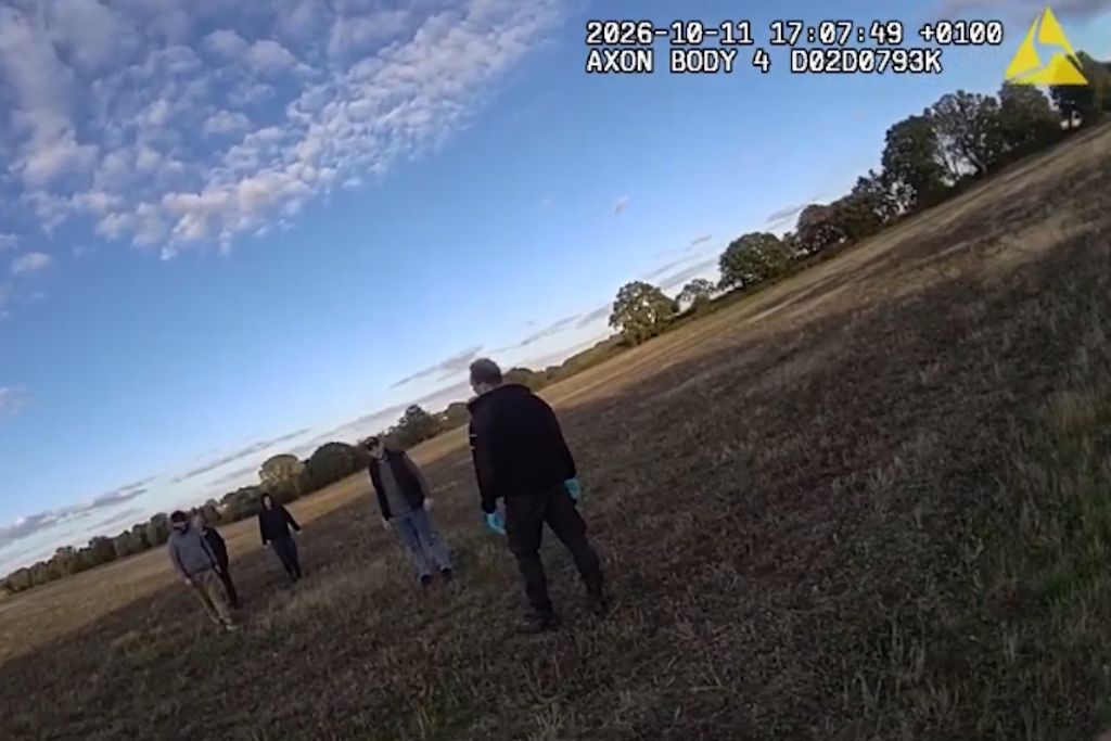 An Essex Police body-worn camera still of a rural engagement officer facing four people standing in a large, open, grassy field at dusk