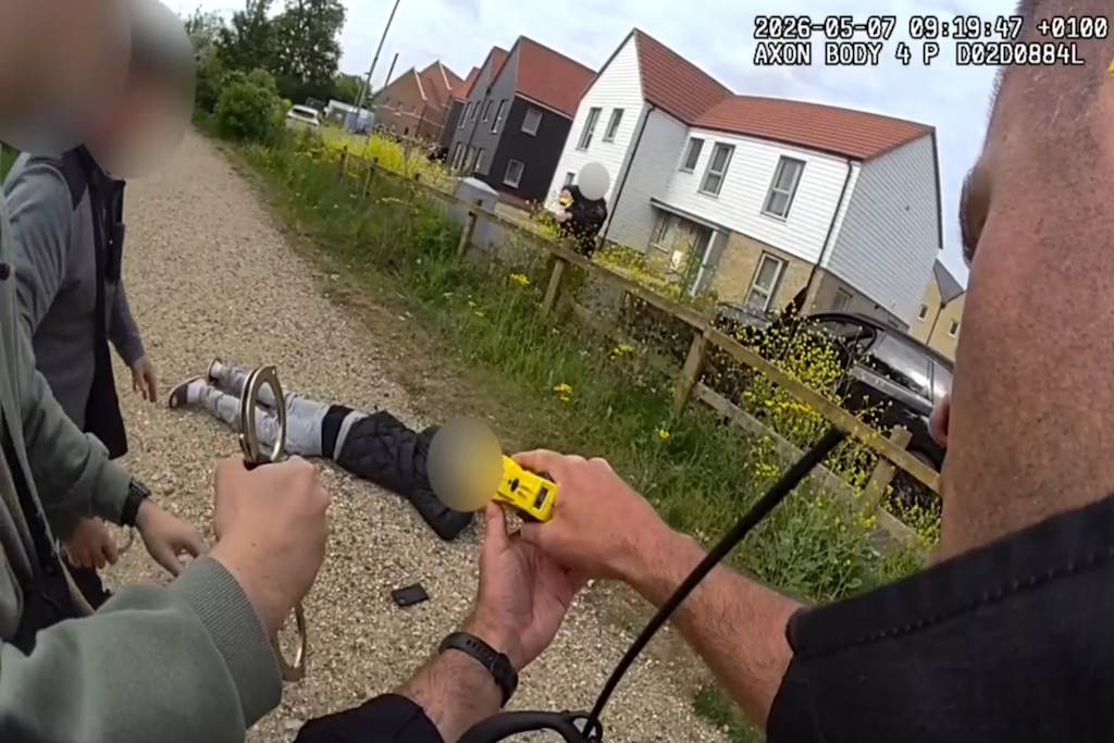 An officer holds a taser towards a suspect who is lying on his front on the ground