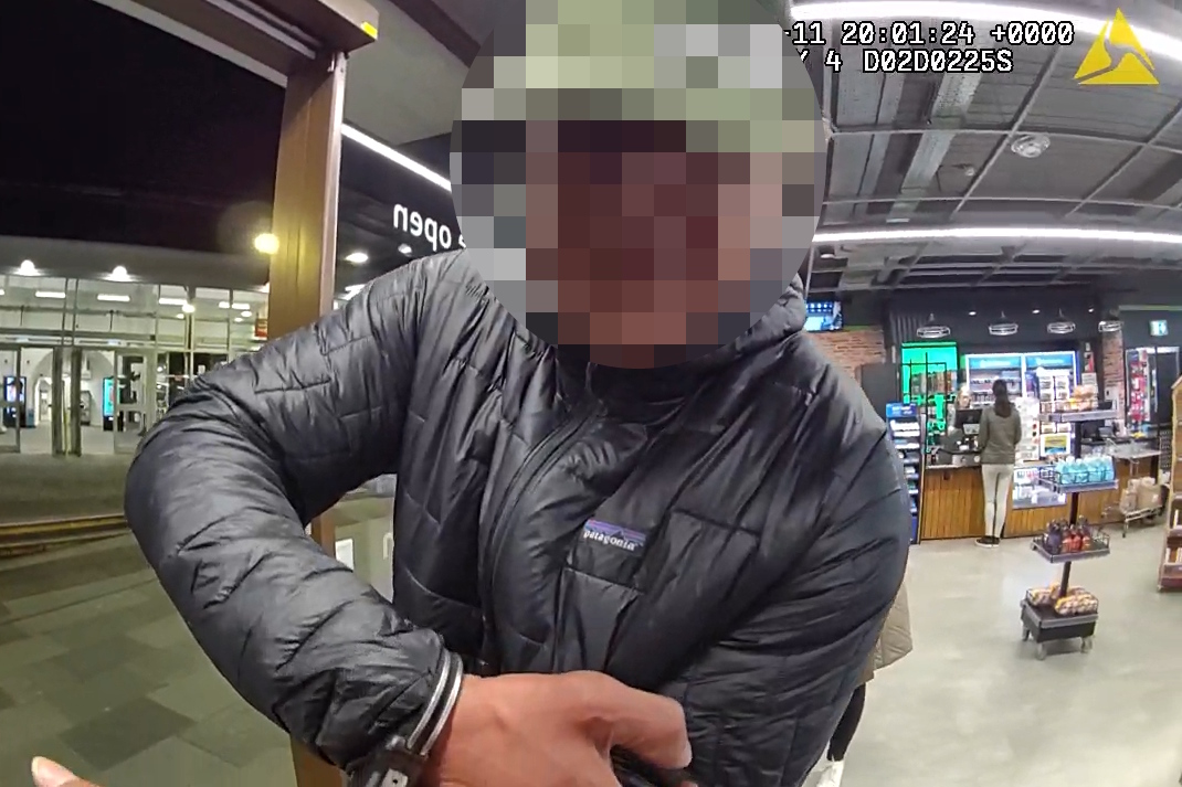 Essex Police body-worn video footage of a person in a black quilted jacket being handcuffed inside a shop at a railway station