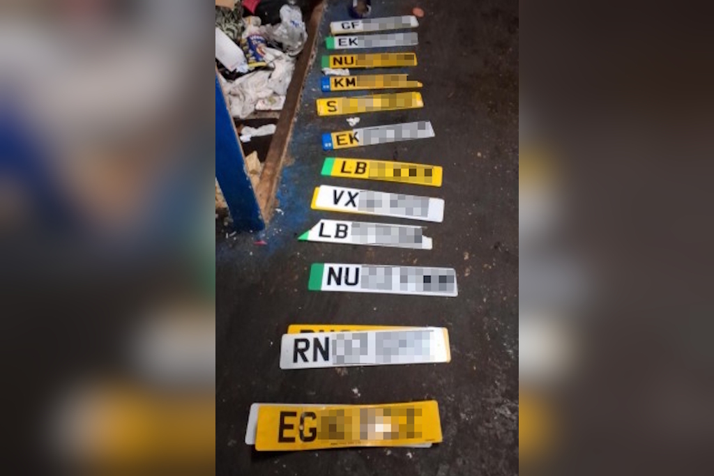 A number of vehicle licence plates laid out on the floor of a garage